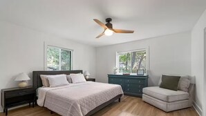 Une chambre à coucher comprenant un lit, des tables de chevet, une commode, une chaise et un ventilateur de plafond.
