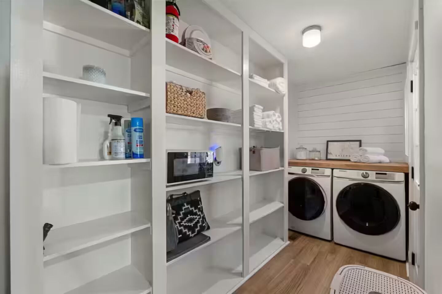 A laundry room with a washing machine, dryer, shelves with cleaning supplies, and a microwave.