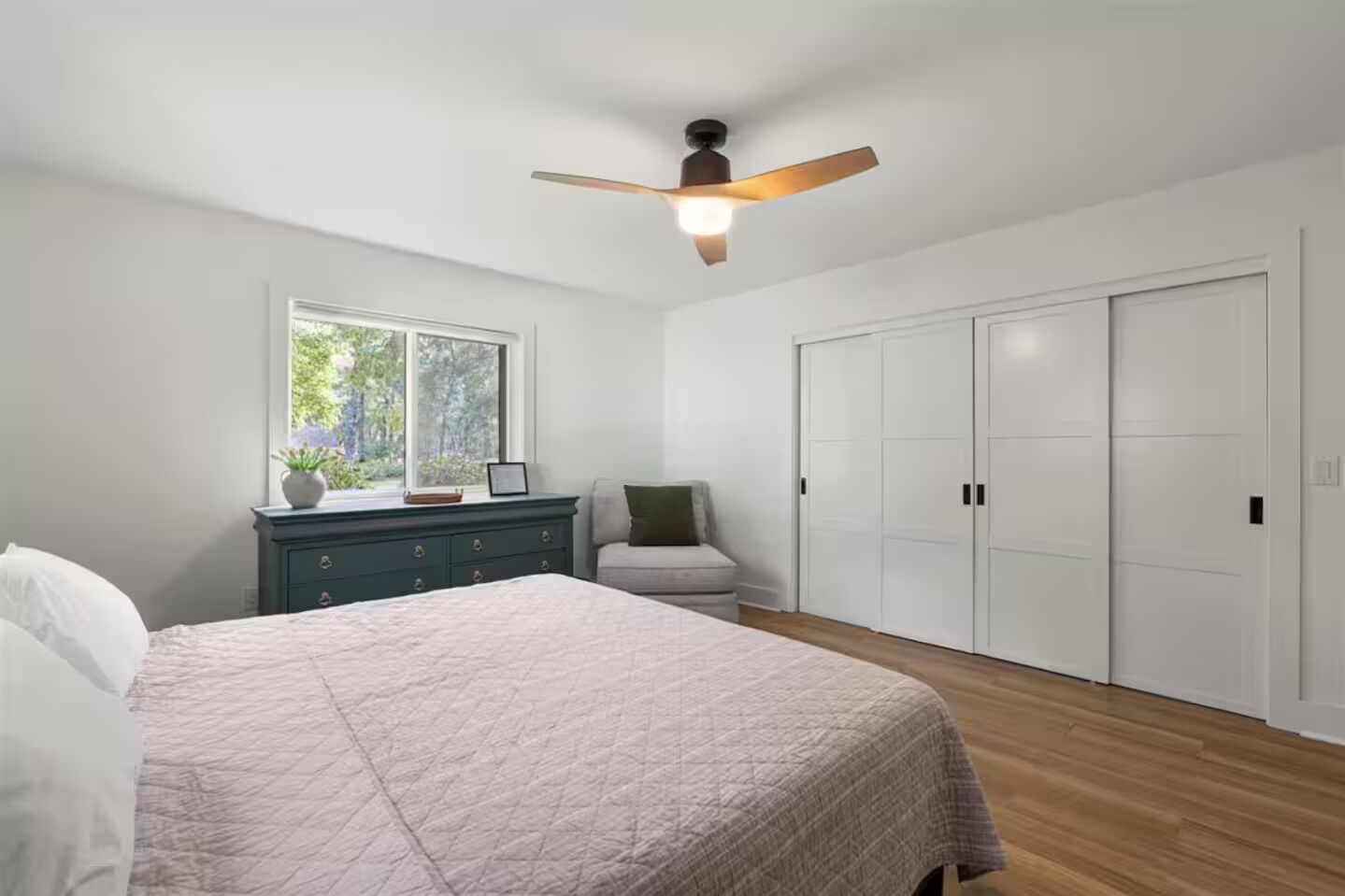 A bedroom with a bed, a dresser, a chair, a window, and a closet.