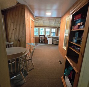 A room with wooden walls, a carpeted floor, a dining table with chairs, a sofa, and a bookshelf with board games. - Family Lake Days - Walk to Beach, Shows, Ice Cream (Mount Gretna)
