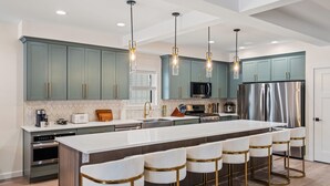 A modern kitchen with a large island, bar stools, stainless steel appliances, and pendant lighting. - Blue Haven 9BR New Lakefront Estate, Dock, Sauna, Elevator, Sleeps 34 (Lake Harmony)