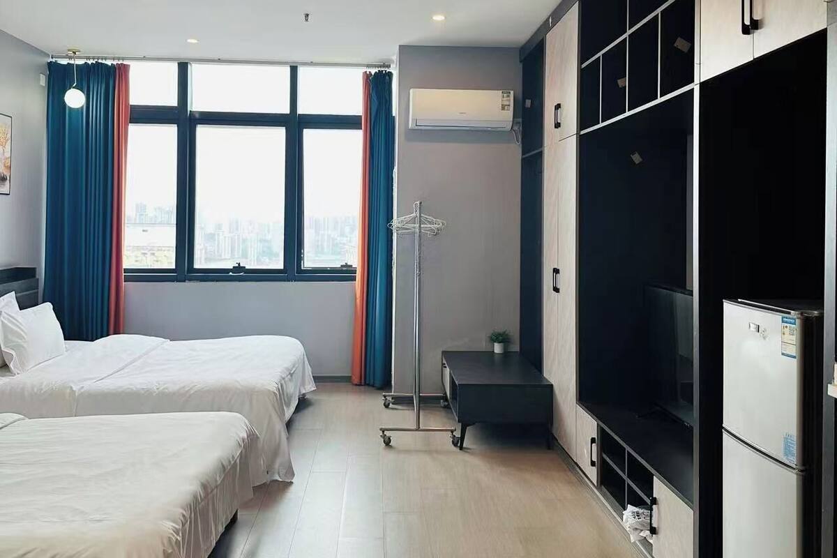 Une chambre d’hôtel avec deux lits, une grande fenêtre, un climatiseur, une armoire et un téléviseur.