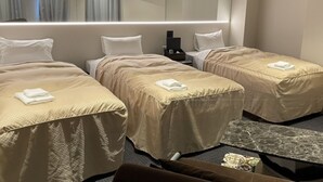 A hotel room with two single beds, a flat-screen TV mounted above a desk, and a small table with a lamp. - HOTEL LiVEMAX Nara Ekimae (Nara)
