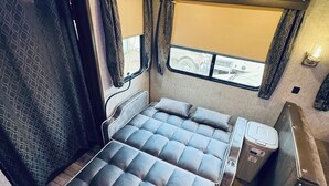 Een compact interieur van een camper, met een bed, een klein tafeltje en een raam.