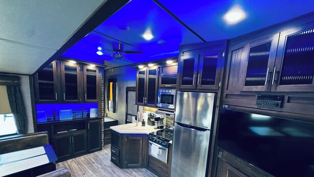Een moderne keuken met donkere houten kasten, roestvrijstalen apparatuur en blauwe sfeerverlichting.