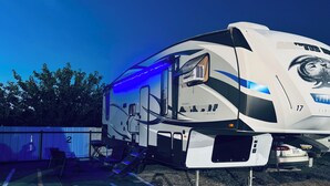 Een grote RV met een overdekte leefruimte, een schuifdeur en een klein bijgebouwtje met een raam.