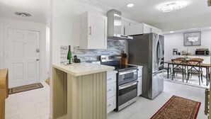 Una cucina moderna con mobili bianchi, un'isola centrale, elettrodomestici in acciaio inossidabile e un'area pranzo con tavolo e sedie in legno.