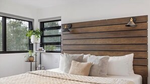 Una camera da letto con un letto grande, una testiera in legno, due lampade a parete e una finestra vista alberi.