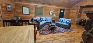 A cozy cabin interior with a wooden floor, two sofas with blue cushions, a dining table, and a fireplace. - Privacy & nature with Hot Tub, Fireplace, fire pit, & local outdoor activities, (Mount Lookout)