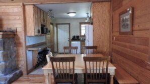A wooden interior with a dining table and chairs, a stone fireplace, and a kitchen area with cabinets and appliances. - Privacy & nature with Hot Tub, Fireplace, fire pit, & local outdoor activities, (Mount Lookout)