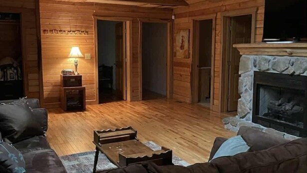 A cozy log cabin interior with a fireplace, a sofa, a coffee table, and a ceiling fan. - Privacy & nature with Hot Tub, Fireplace, fire pit, & local outdoor activities, (Mount Lookout)