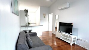 A modern living room with a grey sectional sofa, a flat-screen TV on a white stand, wooden flooring, and a ceiling fan. - Modern 2BR in Highgate Hill near Brisbane CBD (Highgate Hill)
