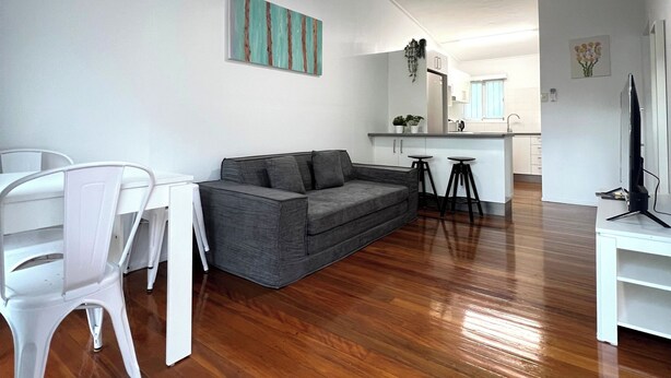 A modern living room with a grey sofa, white dining chairs, a wooden floor, and a ceiling fan. - Modern 2BR in Highgate Hill near Brisbane CBD (Highgate Hill)