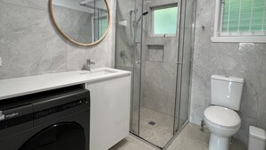 A bathroom with a glass-enclosed shower, a toilet, a sink, and a washing machine. - Modern 2BR in Highgate Hill near Brisbane CBD (Highgate Hill)