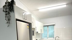 A modern kitchen with white cabinets, a built-in oven, a microwave, and a sink. There are two potted plants on the counter. - Modern 2BR in Highgate Hill near Brisbane CBD (Highgate Hill)