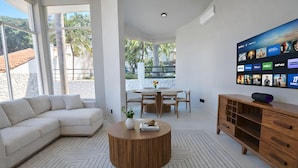 A modern living room with a sectional sofa, a round wooden coffee table, a dining area with a table and chairs, and a flat-screen TV mounted on the wall displaying various streaming services. - Panoramic Paradise Above Puerto Vallarta. Infinity Pool over Romantic Zone
 (Puerto Vallarta)