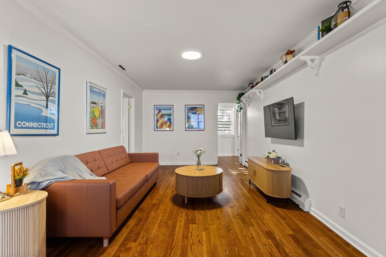 A modern living room with a brown sofa, a round coffee table, and a TV mounted on the wall.