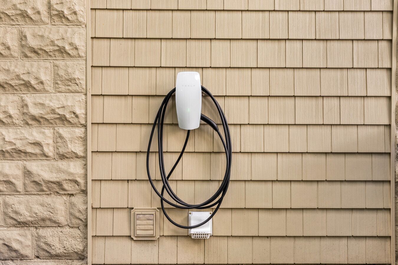 A wall-mounted electrical outlet with a white plug and a black cable.