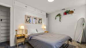 Ein Schlafzimmer mit einem Bett, zwei Nachttischen, einer Ablagefläche, einem Regal mit Pflanzen und einem Spiegel.