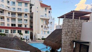 A resort pool area with a stone wall, a thatched umbrella, and a staircase leading to a building with balconies. - LUNA SUITE WITH BALCONY AND OCEAN VIEW IN HOTEL ZONE (Cancún)