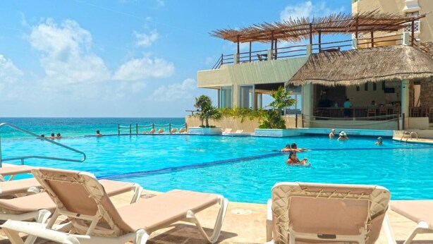 A pool area with lounge chairs, a thatched-roof structure, and a view of the ocean. - LUNA SUITE WITH BALCONY AND OCEAN VIEW IN HOTEL ZONE (Cancún)