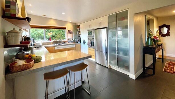 A modern kitchen with a large island, stainless steel appliances, and a view of greenery outside.