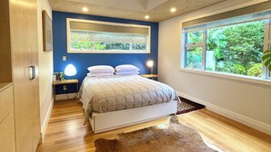 A bedroom with a bed, bedside tables, a hanging light fixture, a window with a view of greenery, and a brown rug.