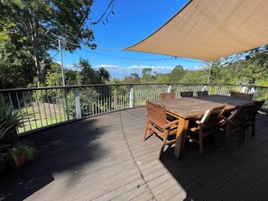 A wooden deck with a table and chairs, surrounded by a white fence and trees. - Beautiful Titirangi Bush & Sea View Santuary with large entertainers deck. (Titirangi)