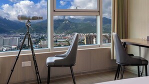A hotel room with a large window offering a cityscape view, a telescope on a tripod, and two modern chairs. - Wonderful Beginning (Tai'an)