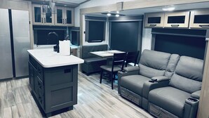 Un intérieur de camping-car compact comprenant un coin cuisine, un espace repas et un coin salon.