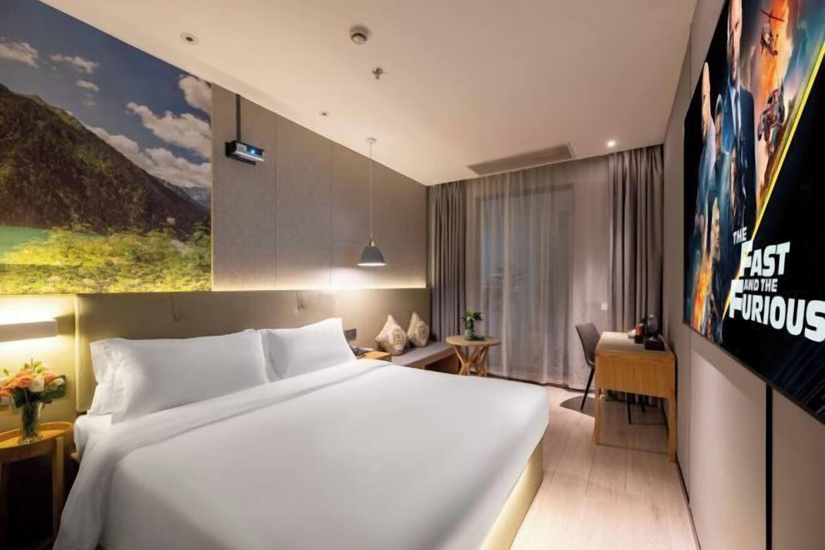A hotel room with a large bed, a desk, a chair, a TV, and a mural on the wall.