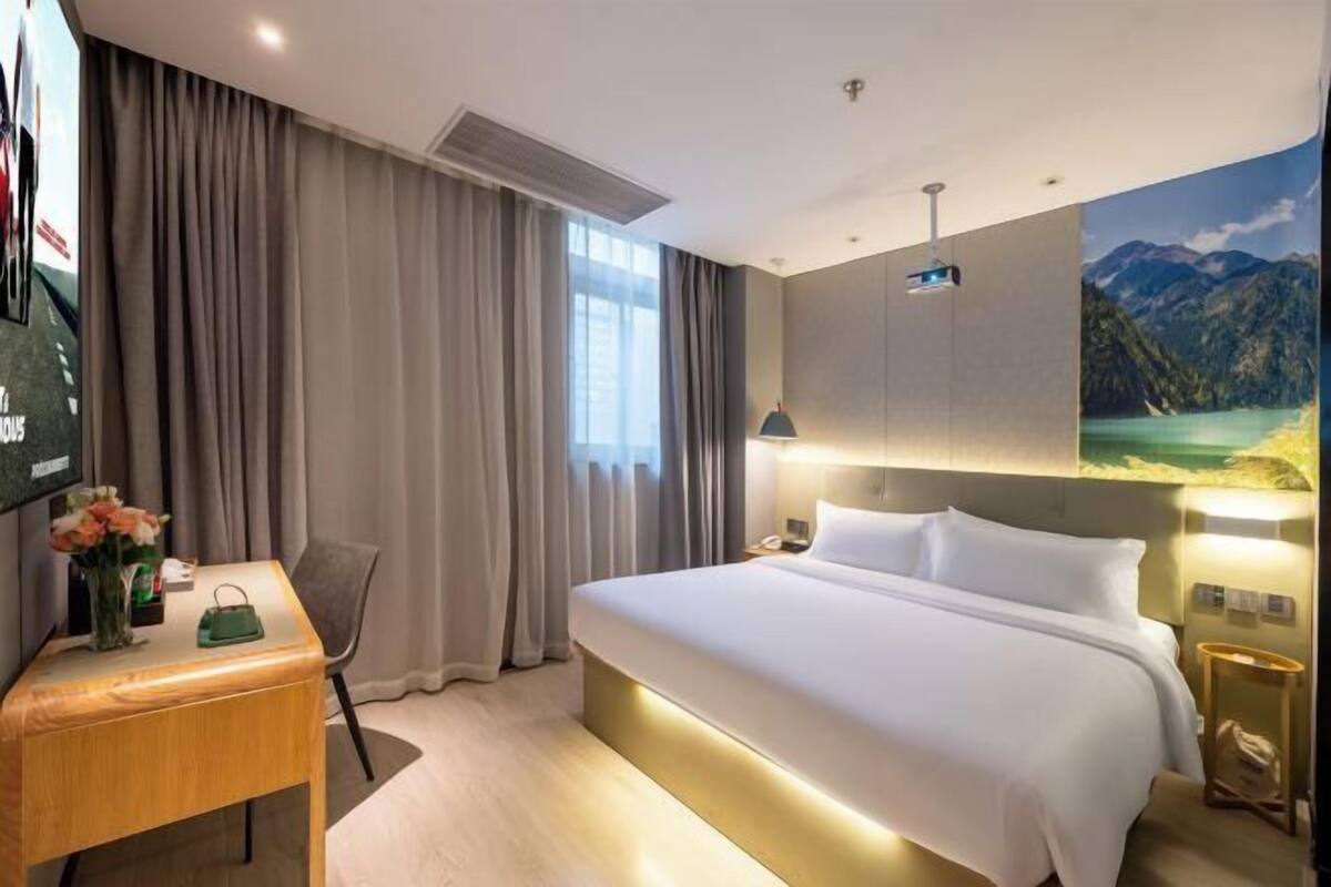 A hotel room with a large bed, a desk with a chair, a TV, and a painting on the wall.