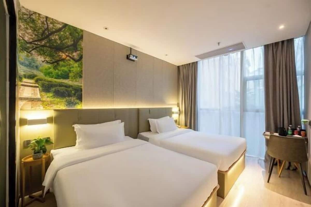 A hotel room with two beds, a desk, a chair, and a large window with curtains.