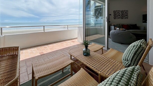 A balcony with wicker furniture, a glass door leading to a living area, and a view of the beach. - Seaview 2beds in the heart of HuaHin BP2 (Hua Hin)