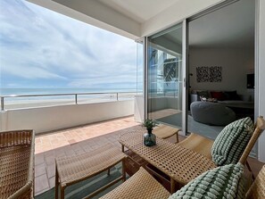 A balcony with wicker furniture, a glass door leading to a living area, and a view of the beach. - Seaview 2beds in the heart of HuaHin BP2 (Hua Hin)