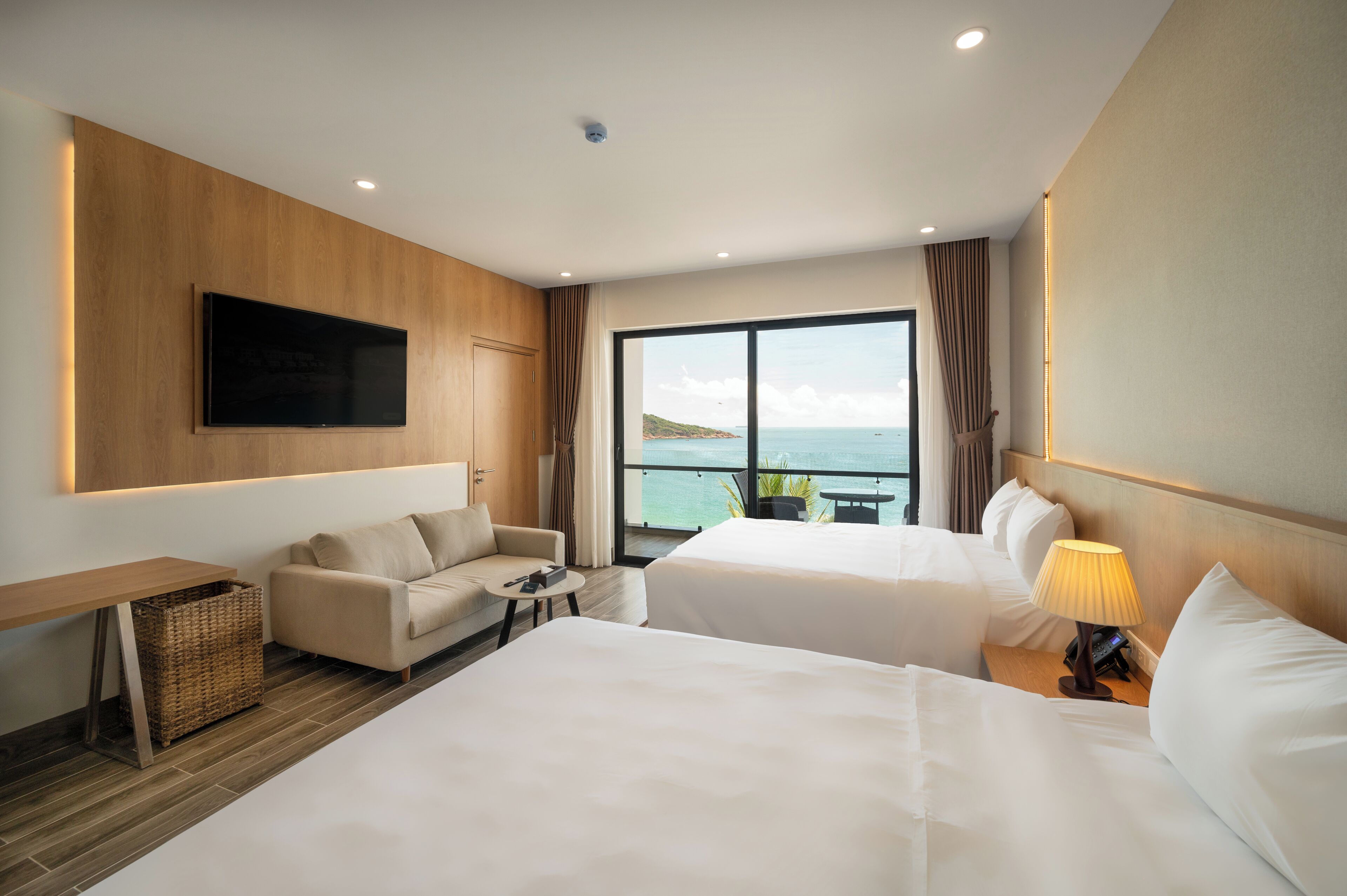 Een hotelkamer met twee bedden, een slaapbank, een televisie en een groot raam met uitzicht op zee.