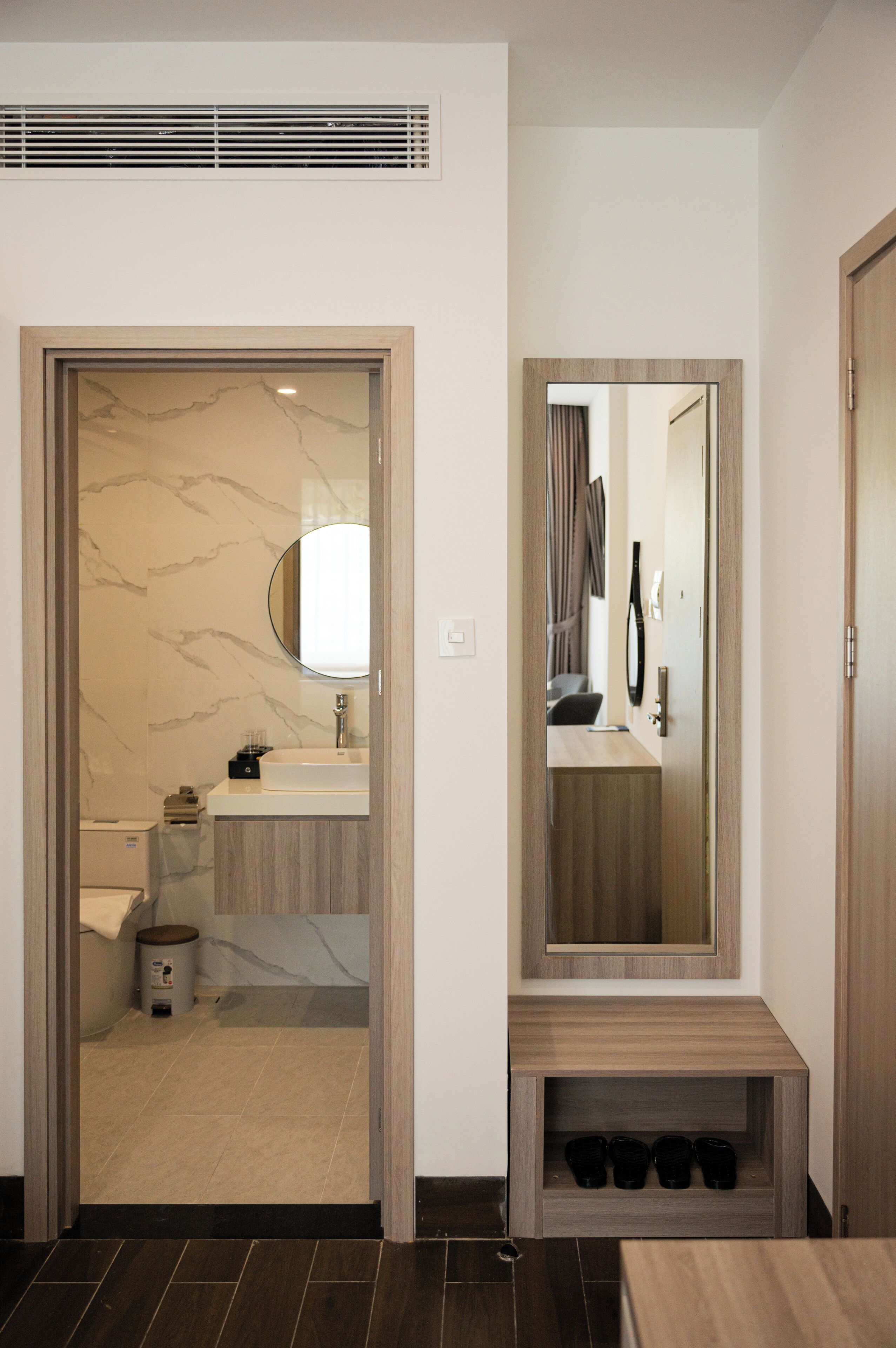 A modern bathroom with a marble wall, a sink, a mirror, and a shelf with black cups.