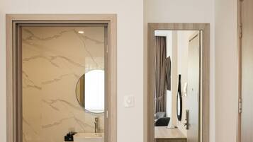 A modern bathroom with a marble wall, a sink, a mirror, and a shelf with black cups.