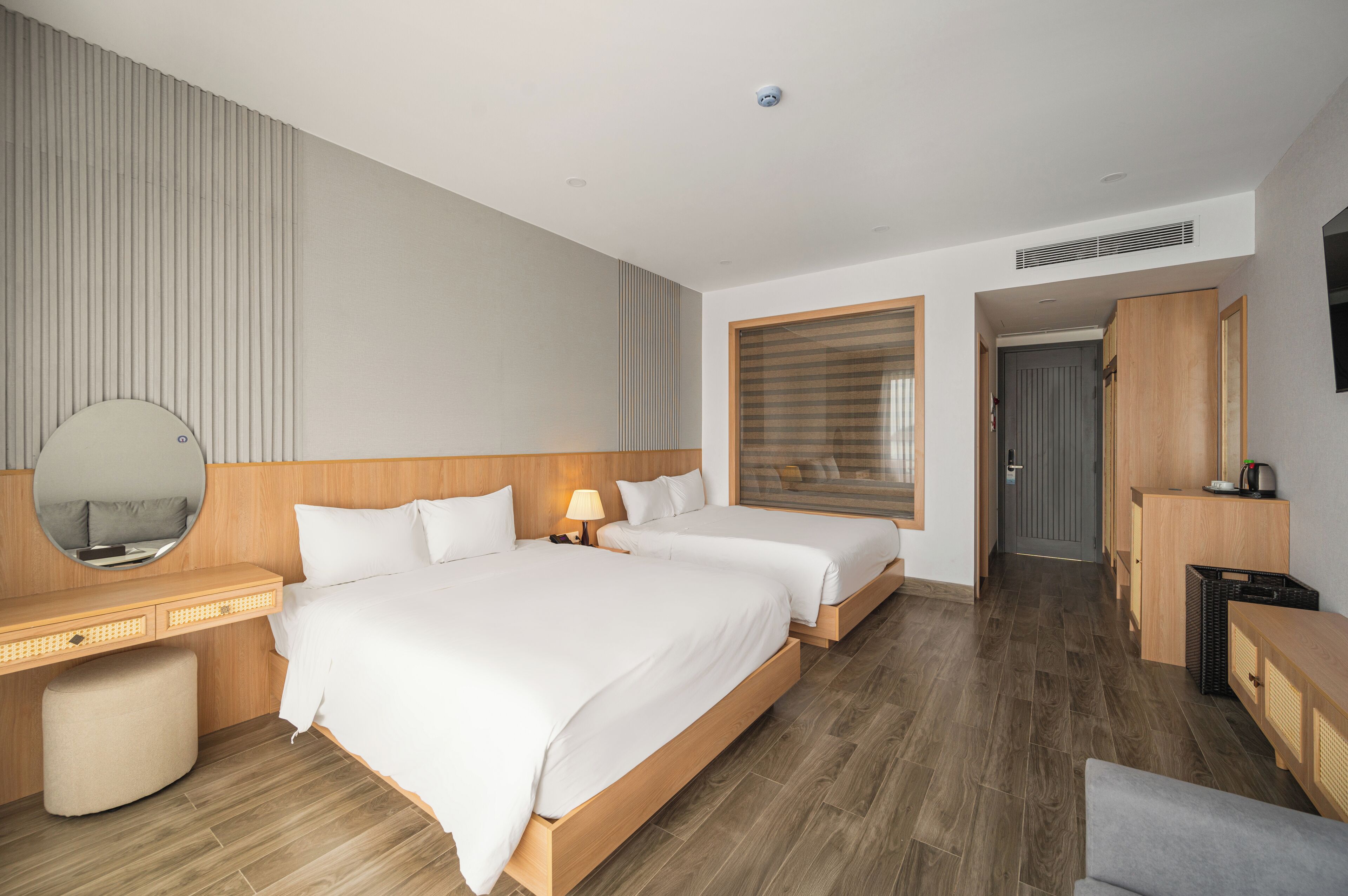 Et moderne hotelværelse med to senge, et træhovedgærde, et rundt spejl, et sengebord og et skrivebord.