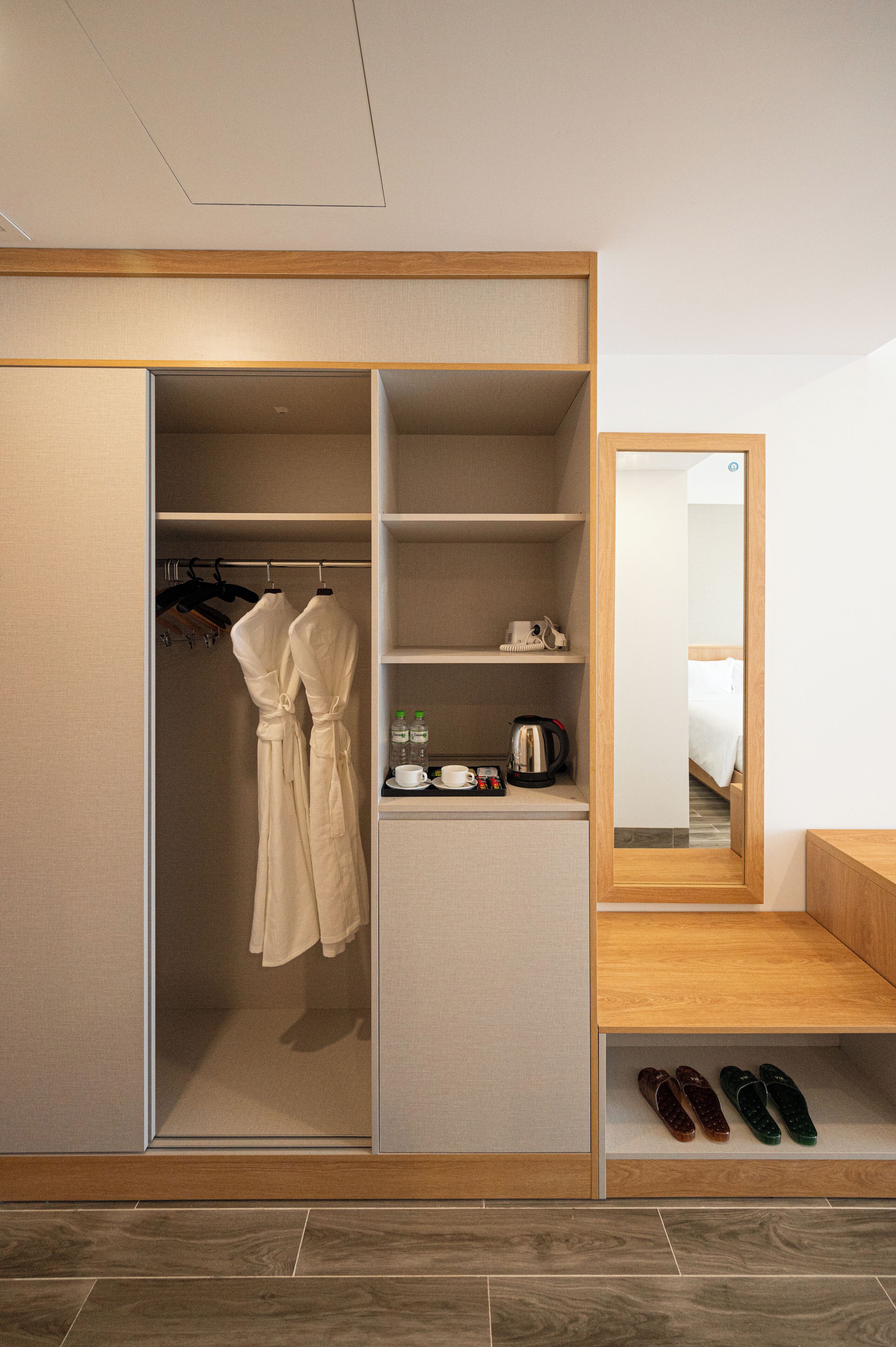 A modern hotel room with a walk-in closet, a mirror, a bed, and a small seating area.
