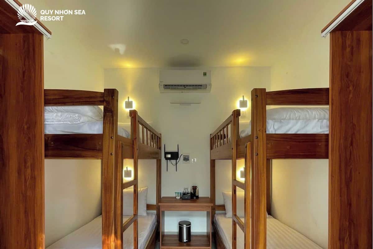 A bunk room with wooden bunk beds, a central table with a trash can, and a wall-mounted air conditioning unit.