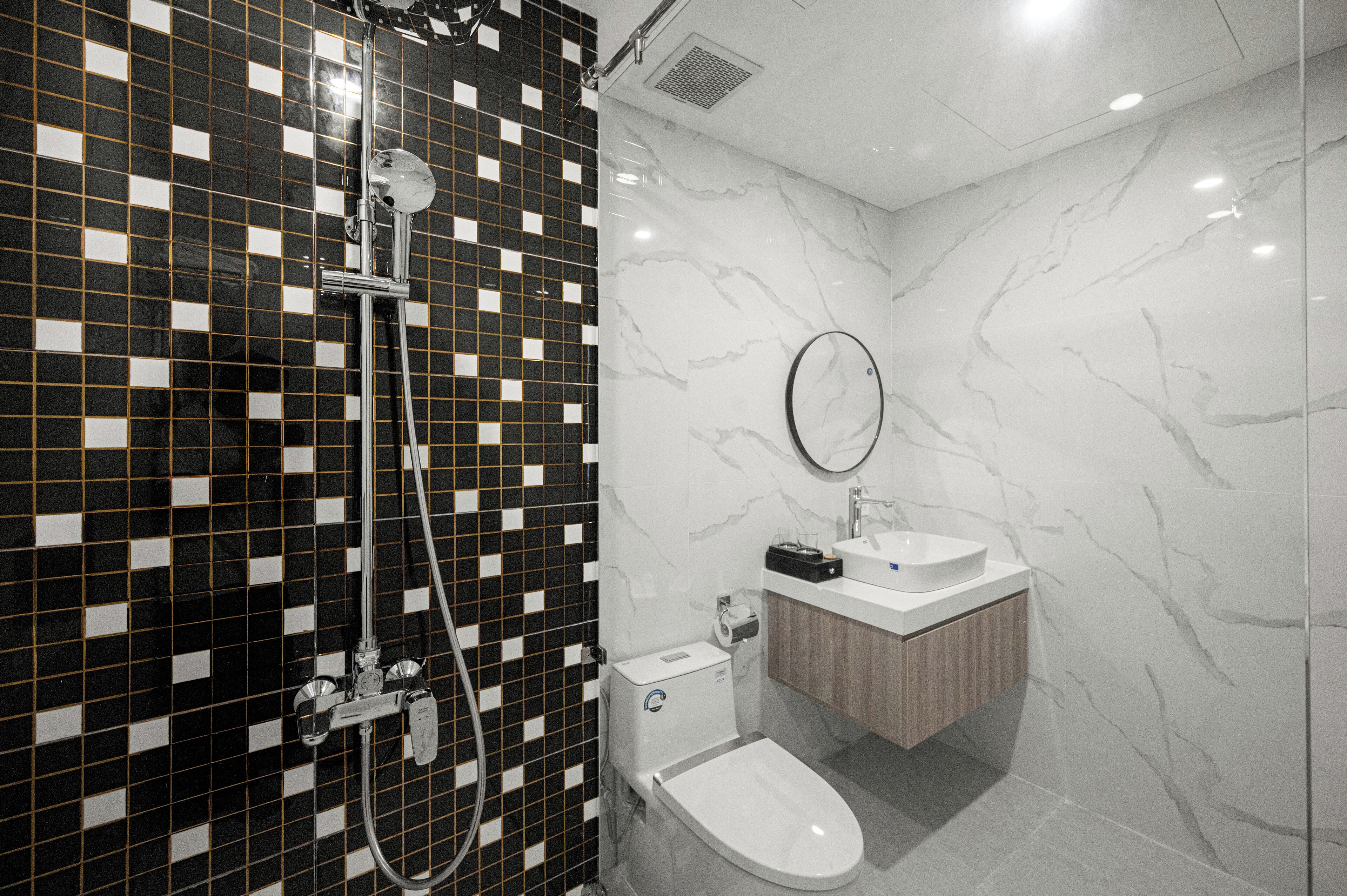 Un baño moderno con baldosas blancas y negras a cuadros, un inodoro blanco, un lavamanos con espejo y una ducha con cabezal de ducha de mano.