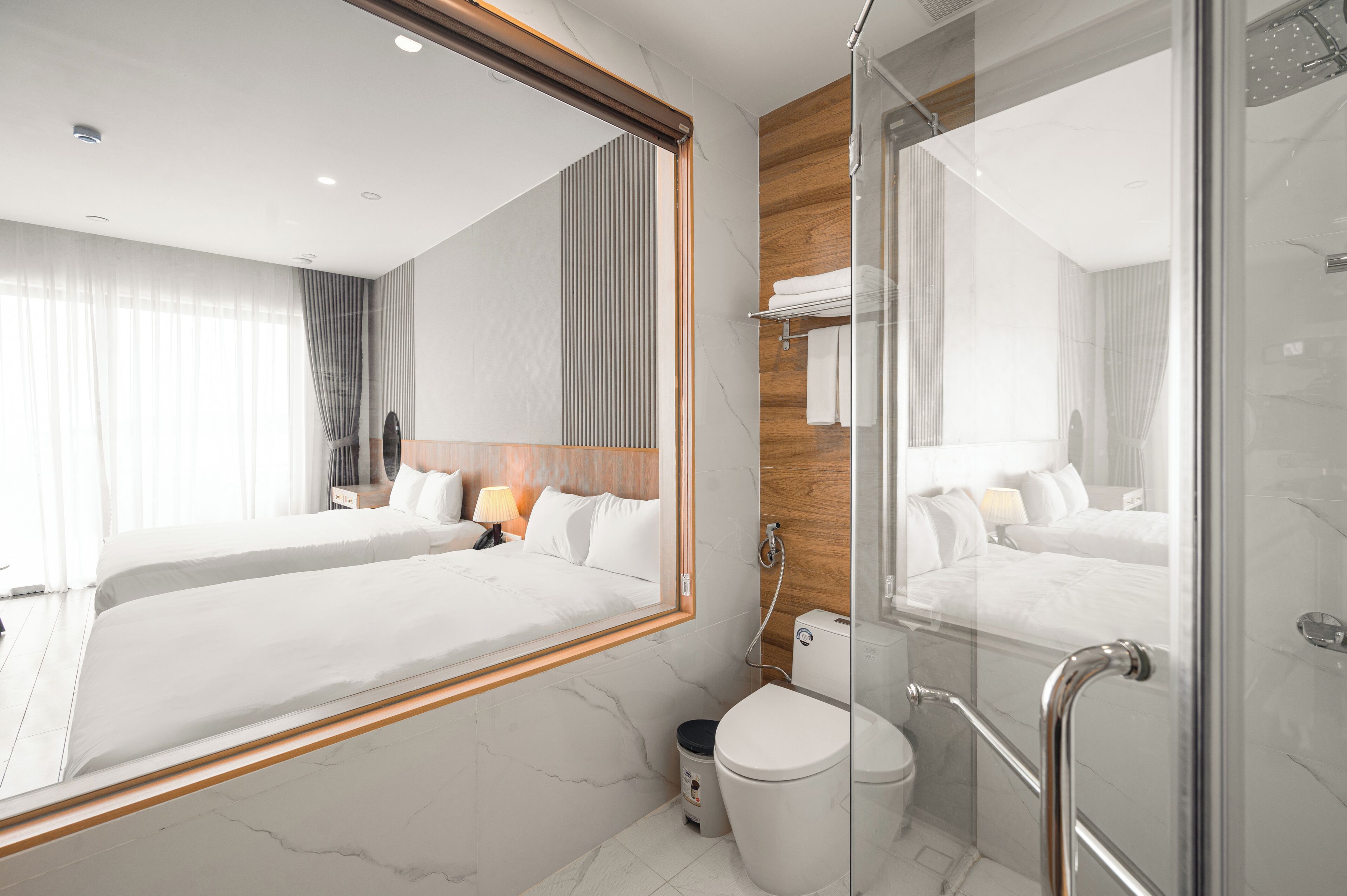 A modern hotel room with a large bed, a glass shower enclosure, and a marble bathroom.