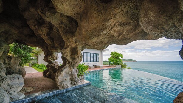 A modern infinity pool with a clear view of the ocean, a white building with large windows, and a natural rock formation overhead. - Quy Nhon Sea Resort (Quy Nhon Nam)