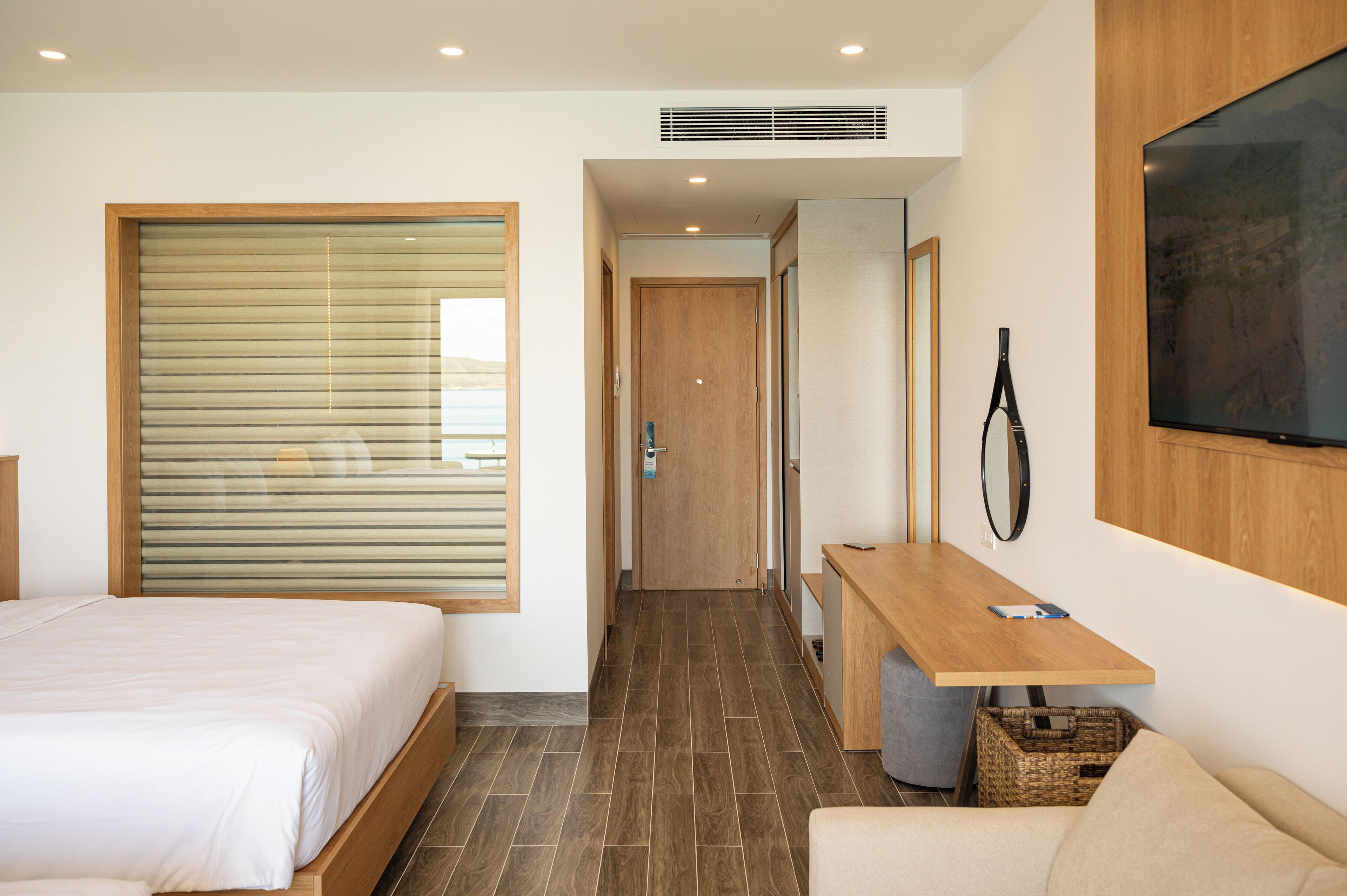Habitación de hotel con cama, escritorio, televisor y ventana grande con persianas.