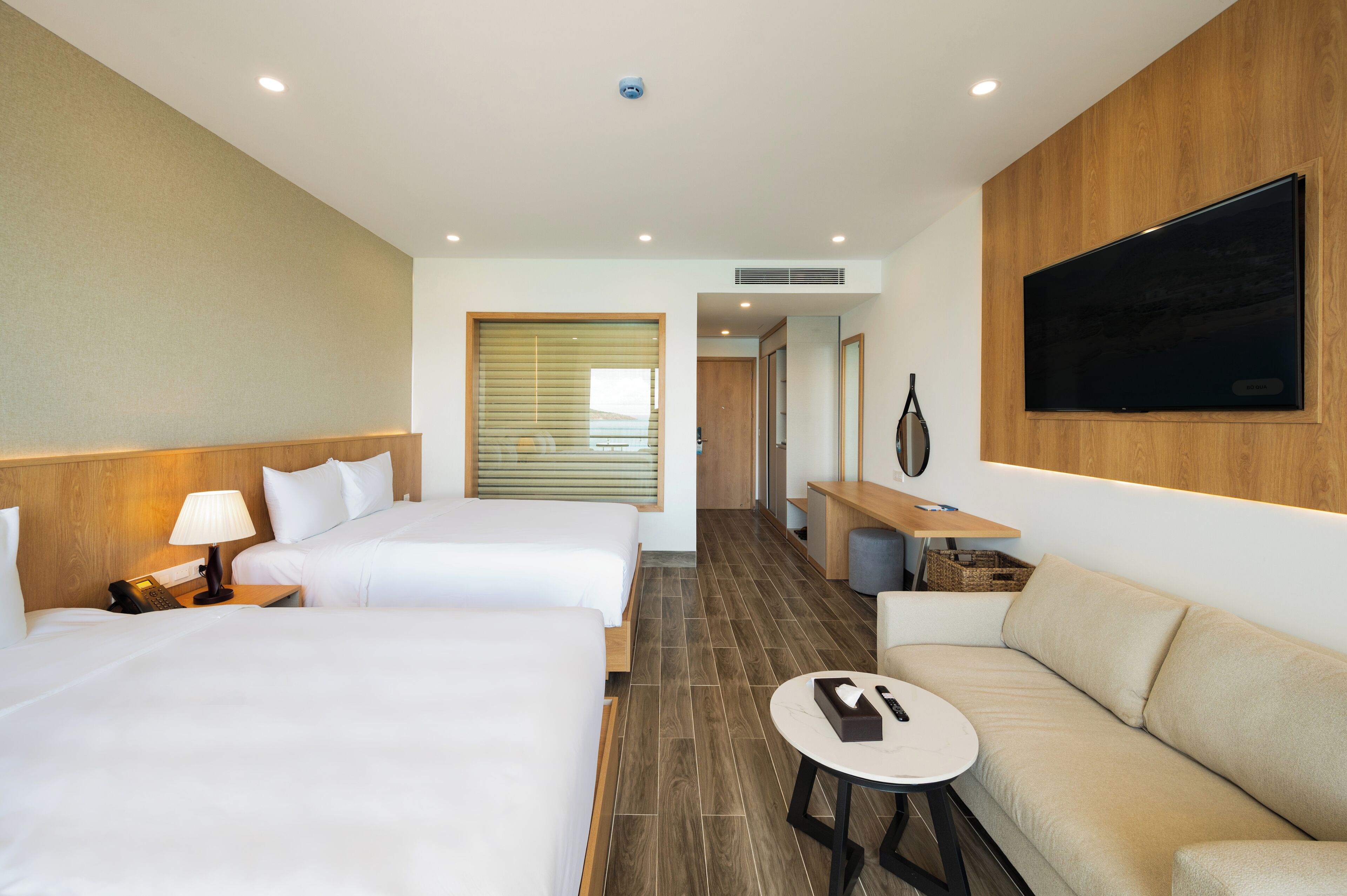 A hotel room with two beds, a sofa, a TV, a desk, and a small table.