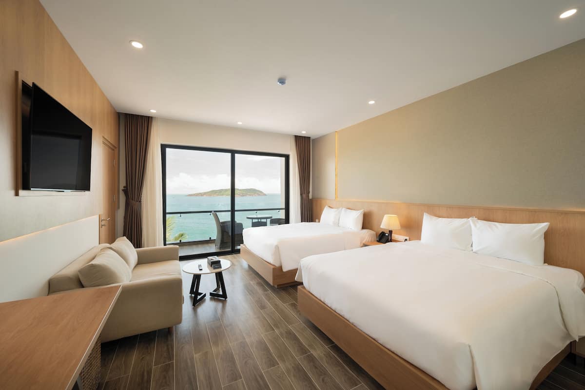 A hotel room with two beds, a sofa, a small table, and a TV mounted on the wall.
