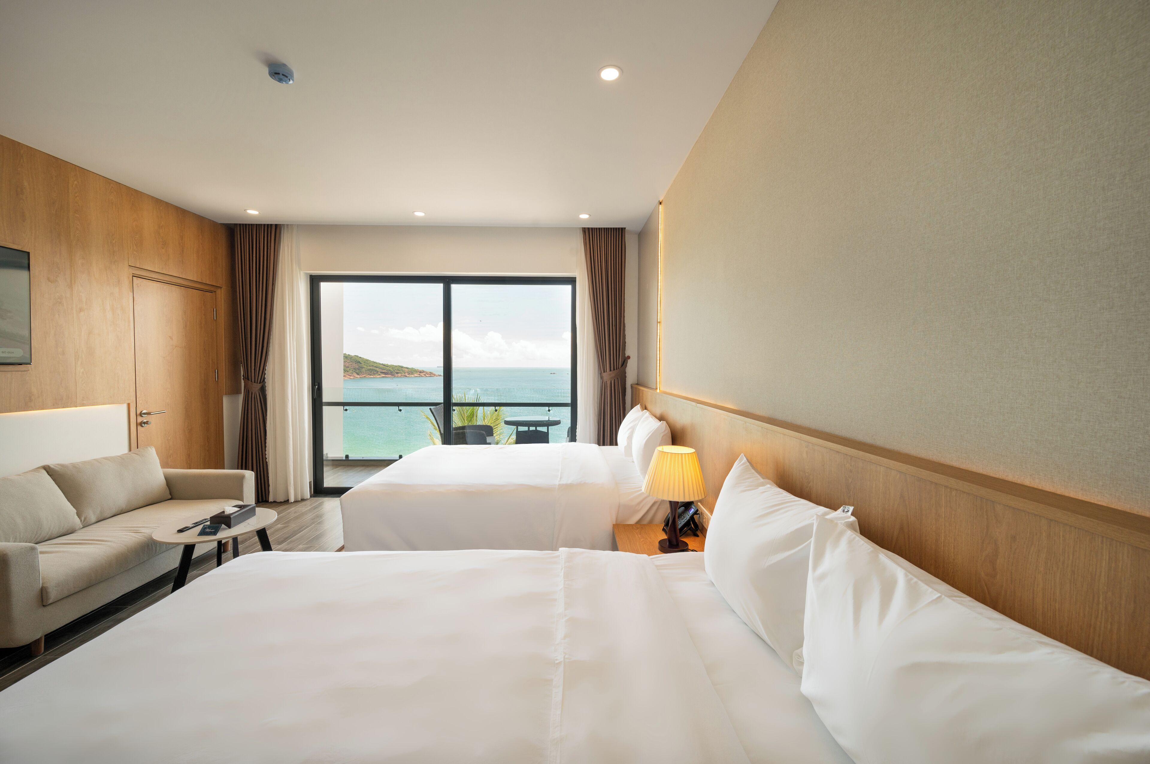Habitación de hotel con dos camas, un sofá, una mesita y vista al mar.