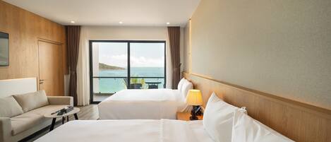 Habitación de hotel con dos camas, un sofá, una mesita y vista al mar.