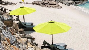 A beach with clear blue water, rocky outcrops, and a hill in the background. There are yellow umbrellas and lounge chairs. - Quy Nhon Sea Resort (Quy Nhon Nam)